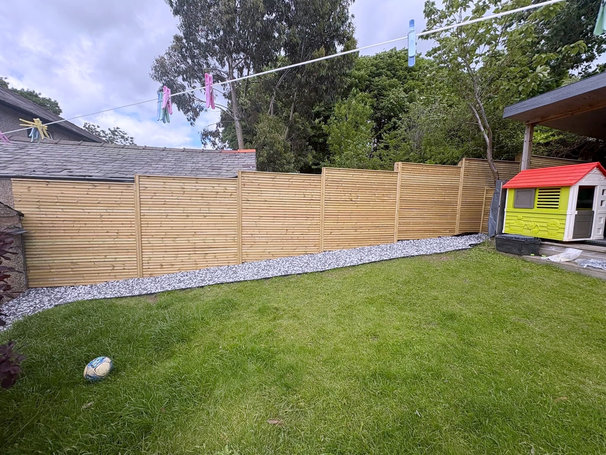 Run of horizontal slatted timber fence along a lawn