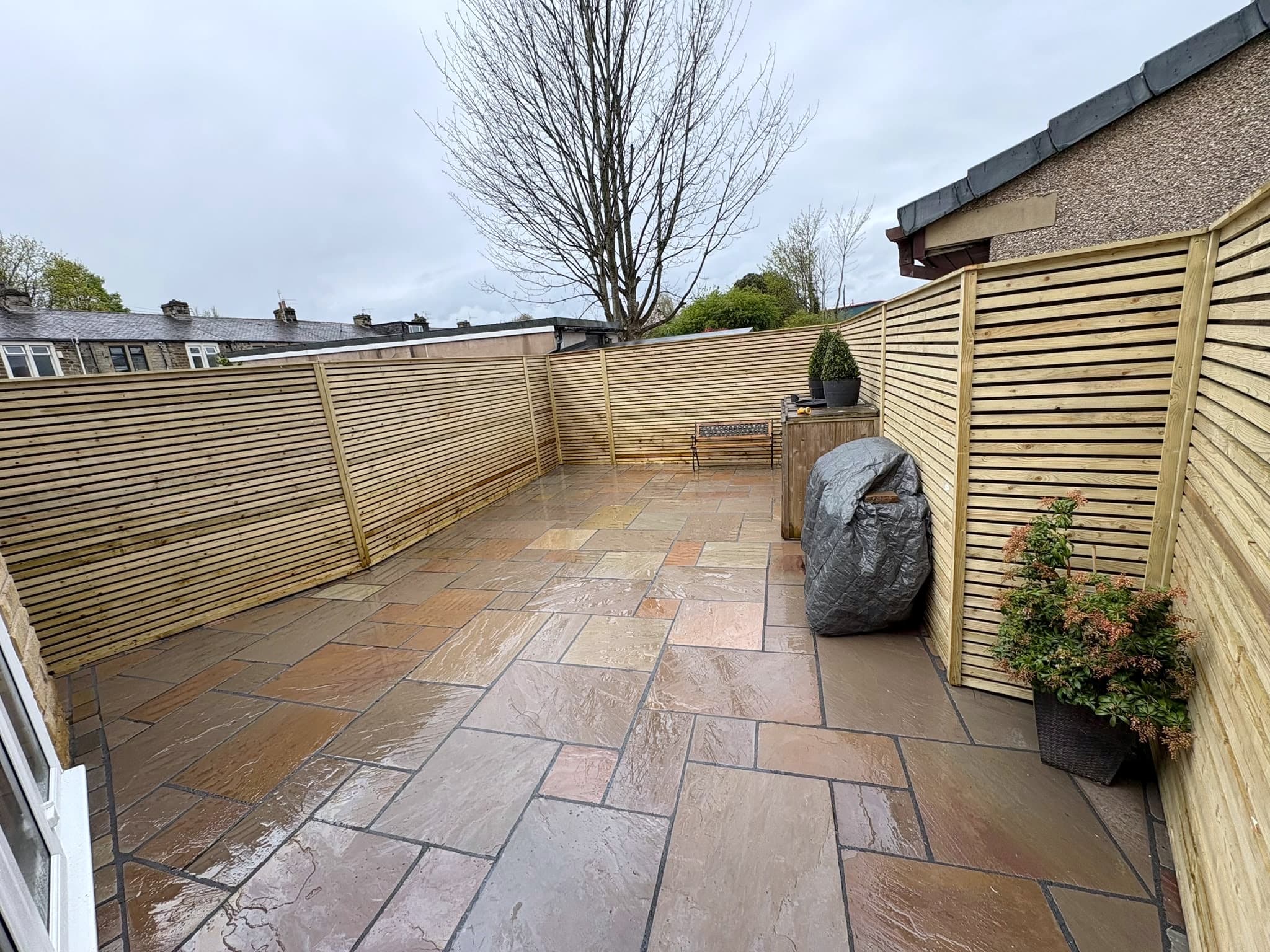 Slatted timber fence enclosing a new sandstone patio with a garden bench