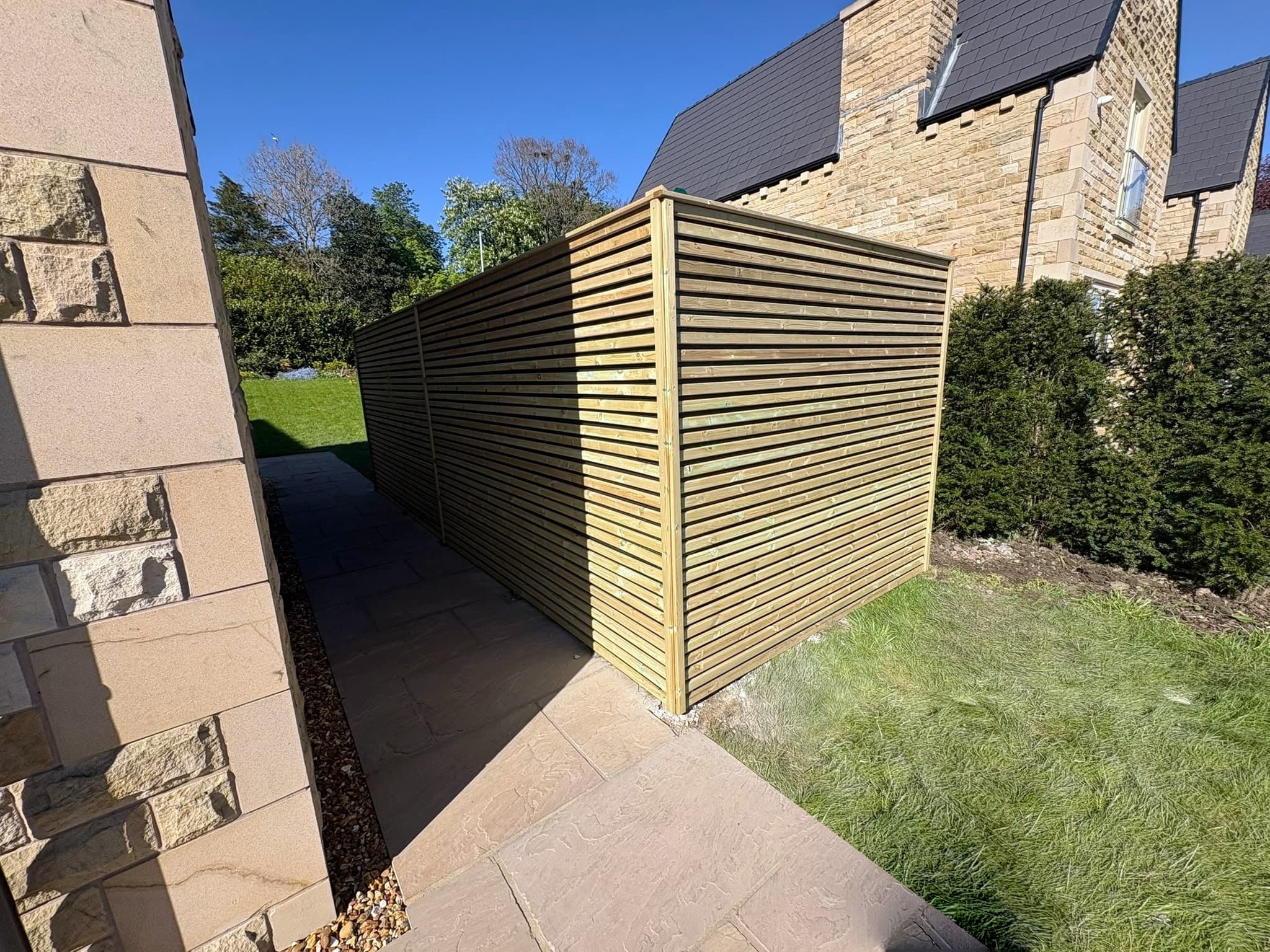 Horizontal slatted timber screen fence beside a paved side path