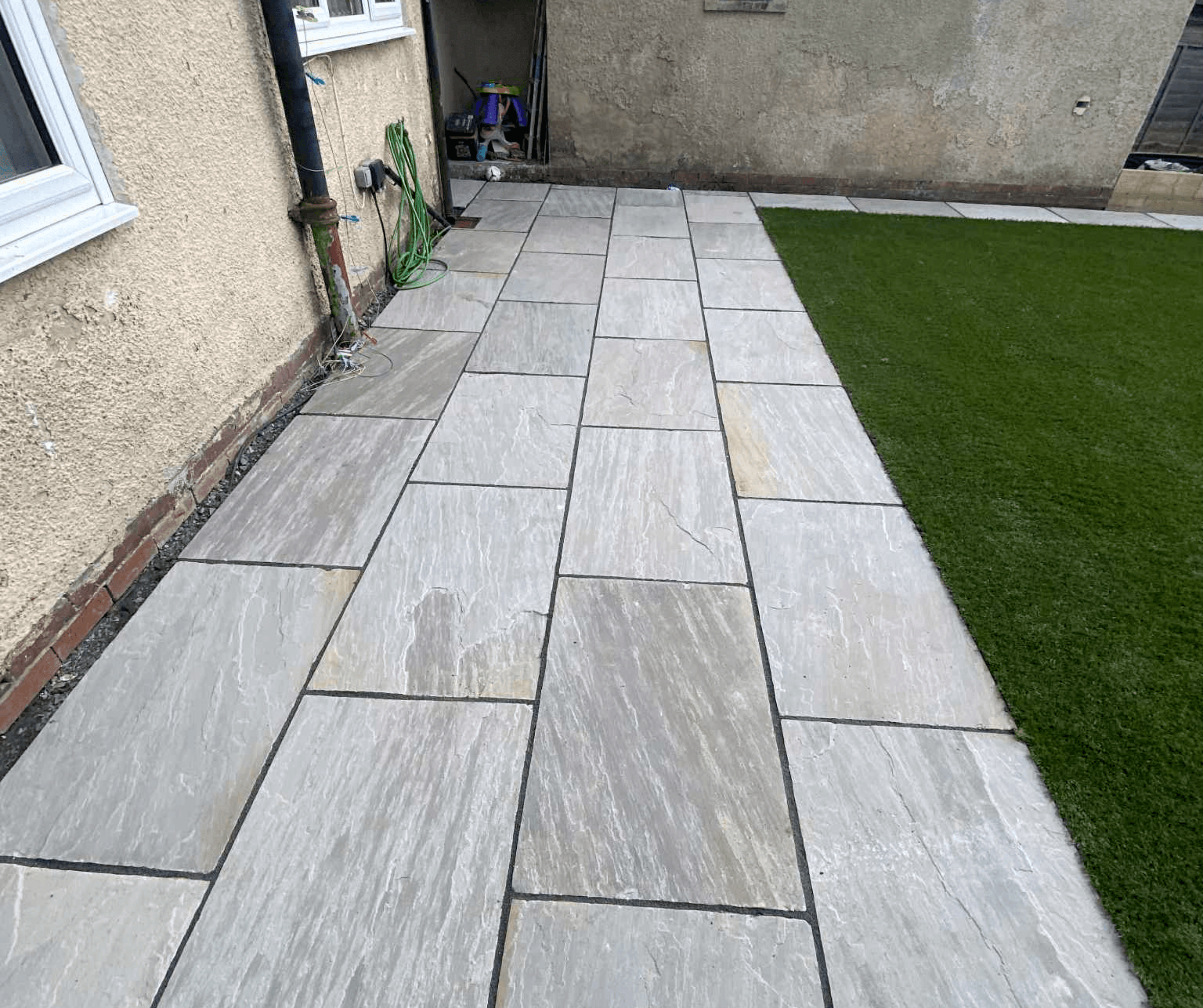 Grey slab patio path running alongside artificial grass