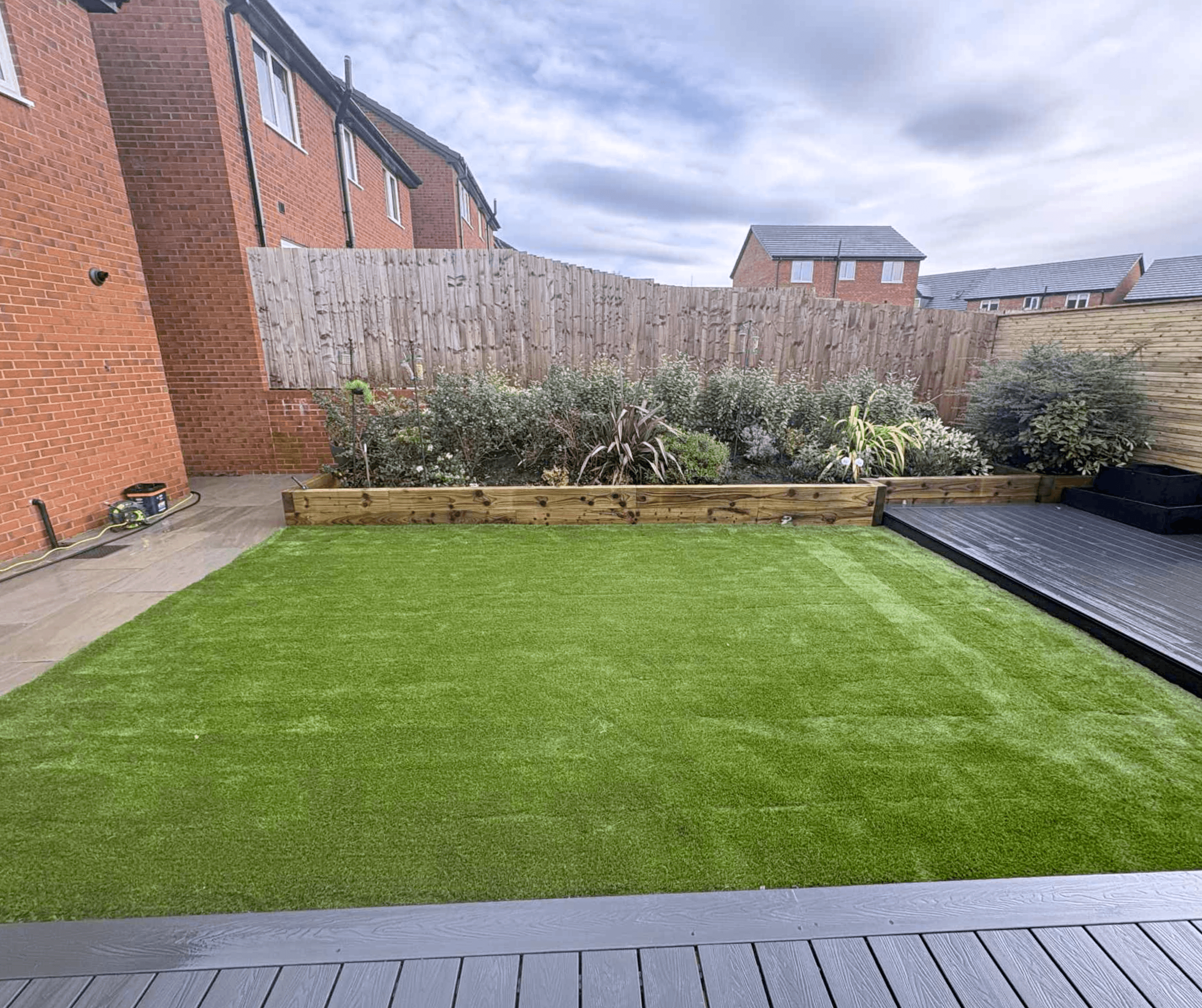 Timber sleeper raised bed with planting beside an artificial grass lawn and dark decking