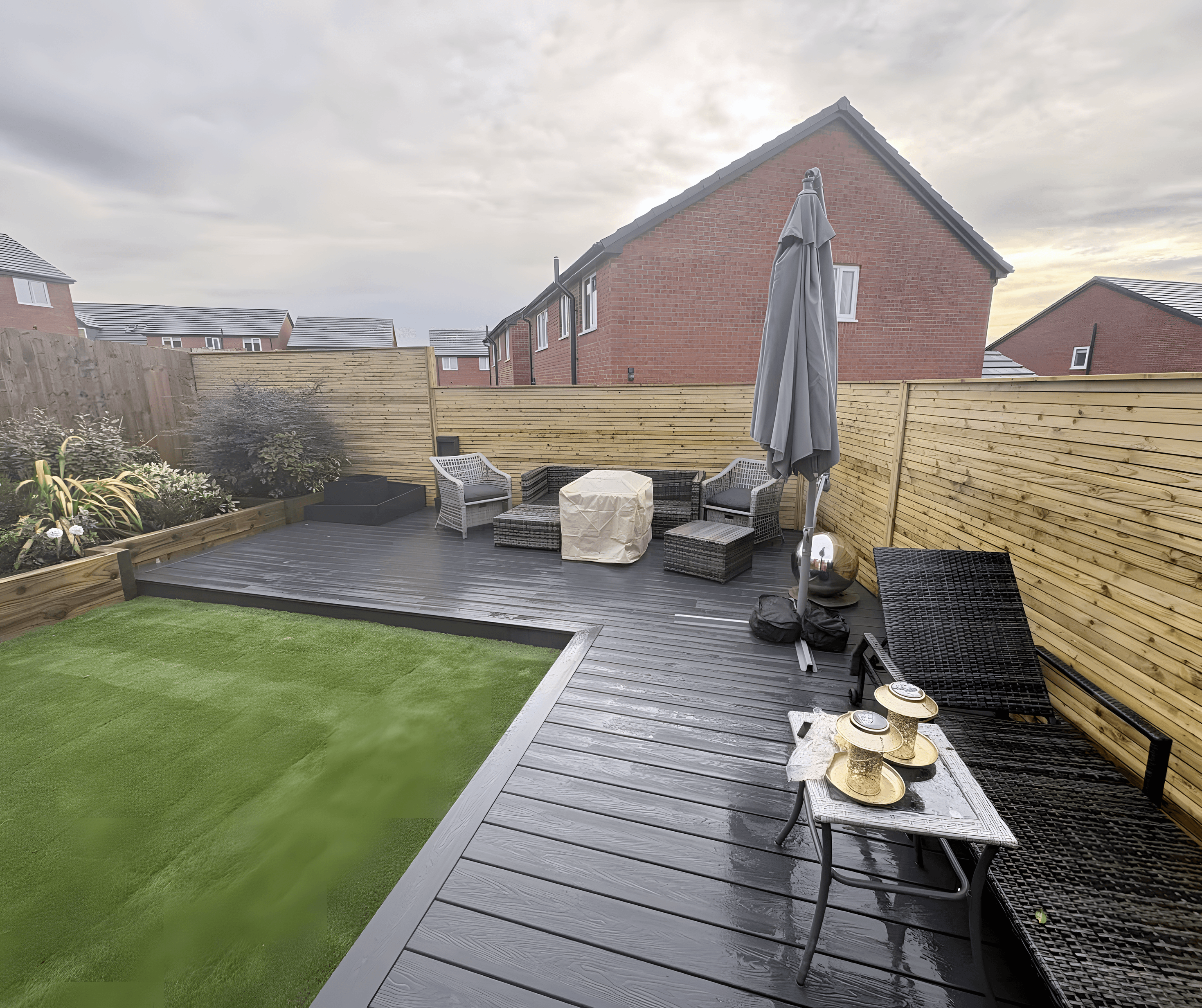 Grey composite decking beside artificial grass in a fenced garden