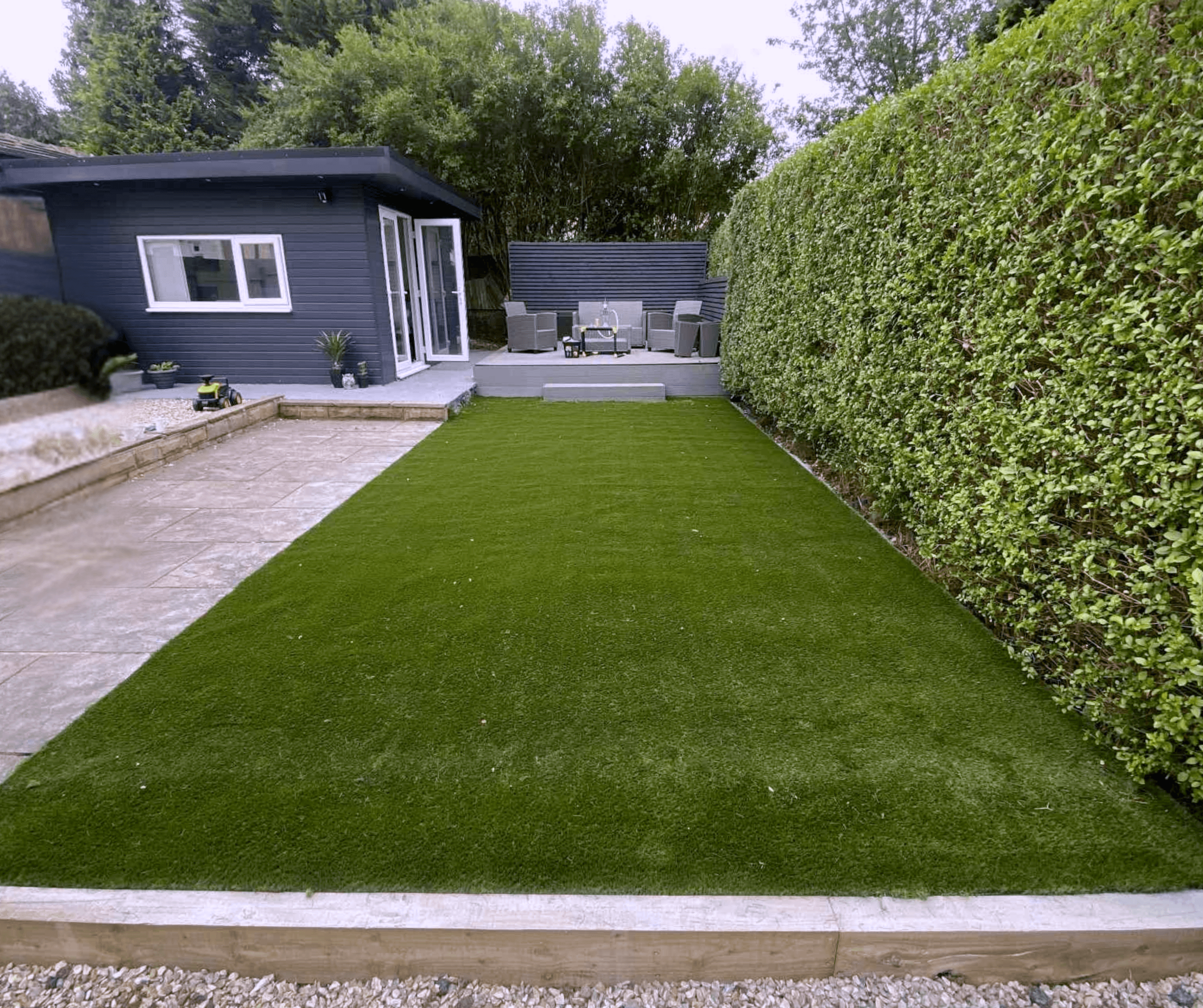 Long artificial grass lawn between a hedge and a slab path