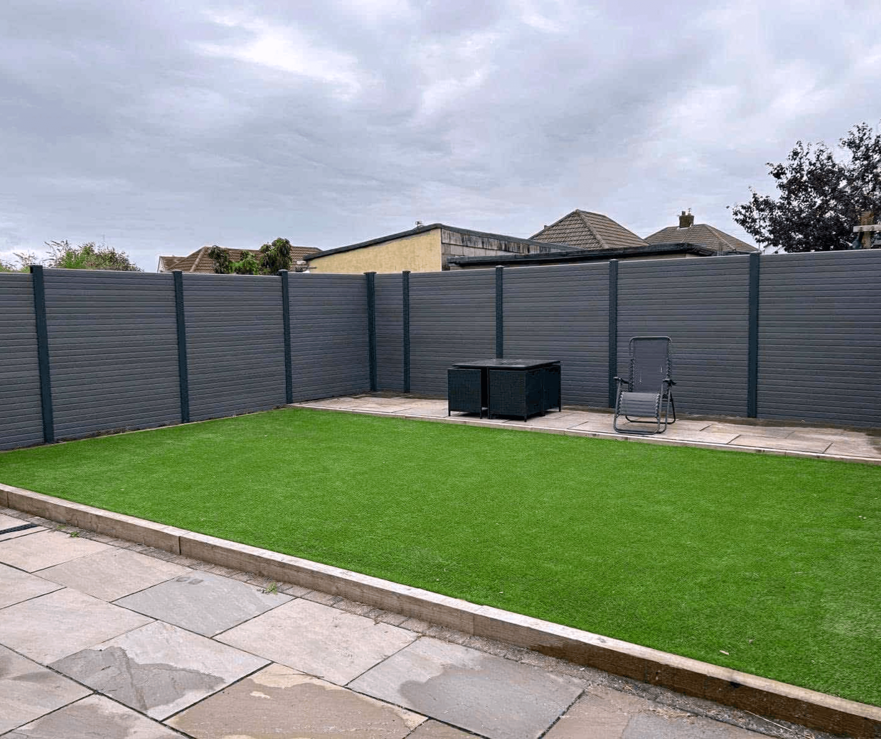 Grey composite fencing around a lawn of artificial grass and a slab patio