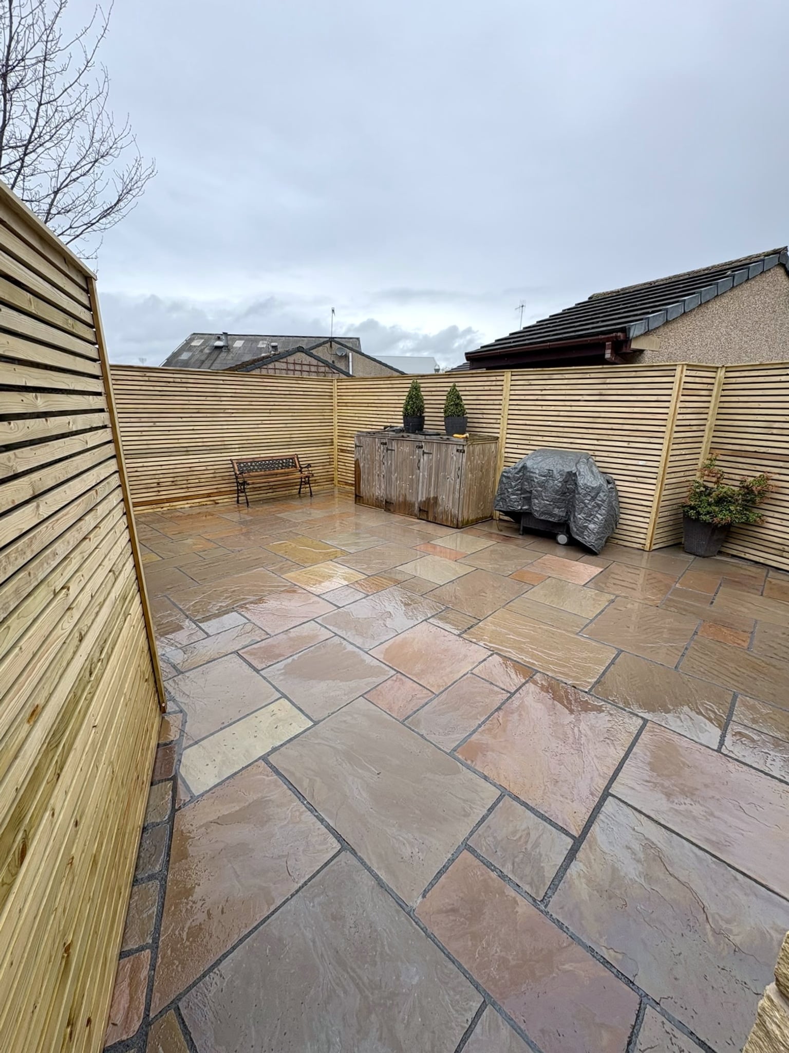 Corner of a slatted timber fence around a sandstone patio