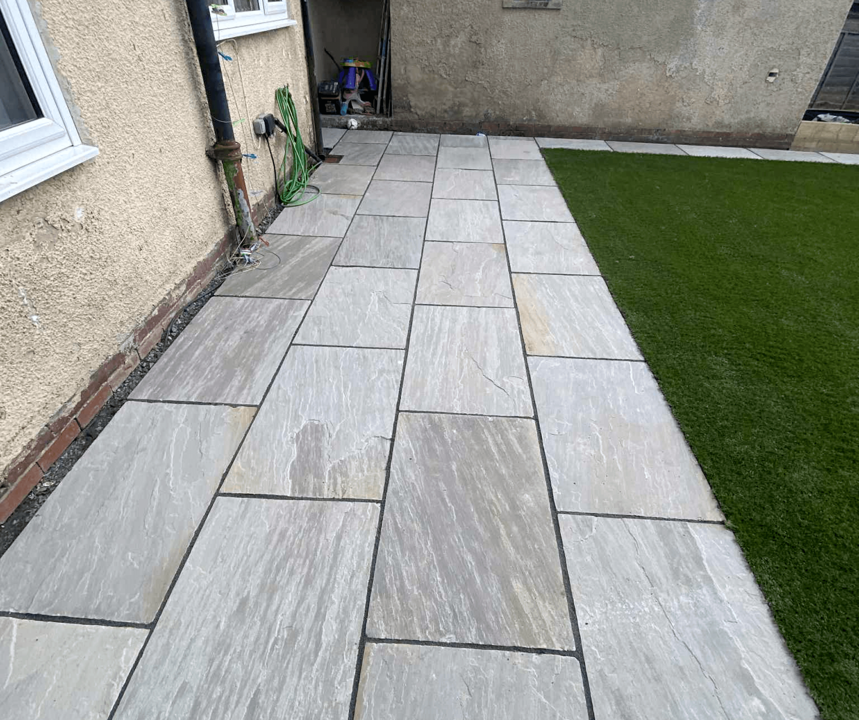 Grey slab patio path running alongside artificial grass